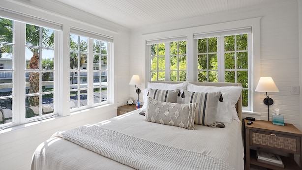 A bedroom with a large bed, two bedside tables, a nightstand, and a window with a view of greenery.
