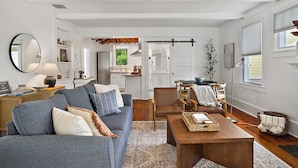 A spacious living area with a sofa, coffee table, and a dining table. There is a kitchen in the background with a sliding door.