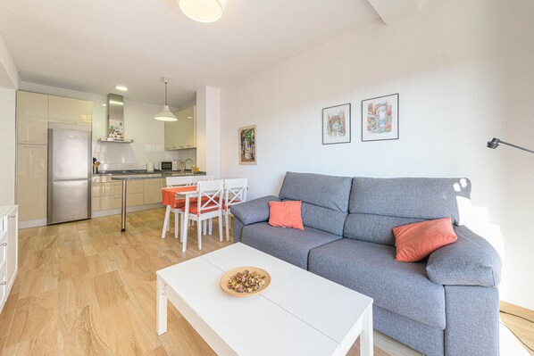 Un salon moderne avec un canapé gris, une table basse blanche et un coin repas comprenant une table et des chaises blanches.
