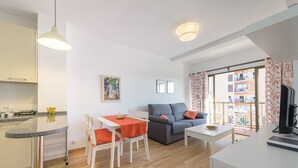 Un appartement moderne comprenant une cuisine, un coin repas et un salon. Il dispose également d’un balcon avec vue sur les immeubles.