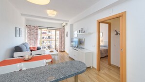 Un salon moderne comprenant un coin repas, un téléviseur et donnant sur le balcon extérieur.