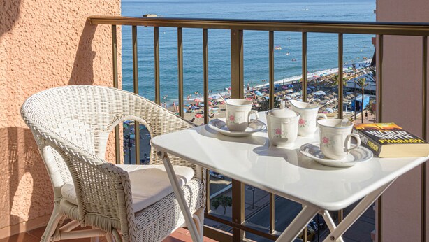Un balcon avec des fauteuils en osier, une table avec des tasses et des soucoupes à thé, et un livre intitulé « Pharaon  » de Wilbur Smith.