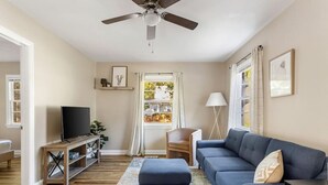 A living room with a TV, sofa, ottoman, and a ceiling fan.