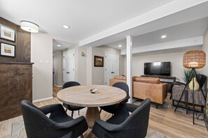 A modern living room with a round table, dark chairs, a TV, and a decorative lamp.
