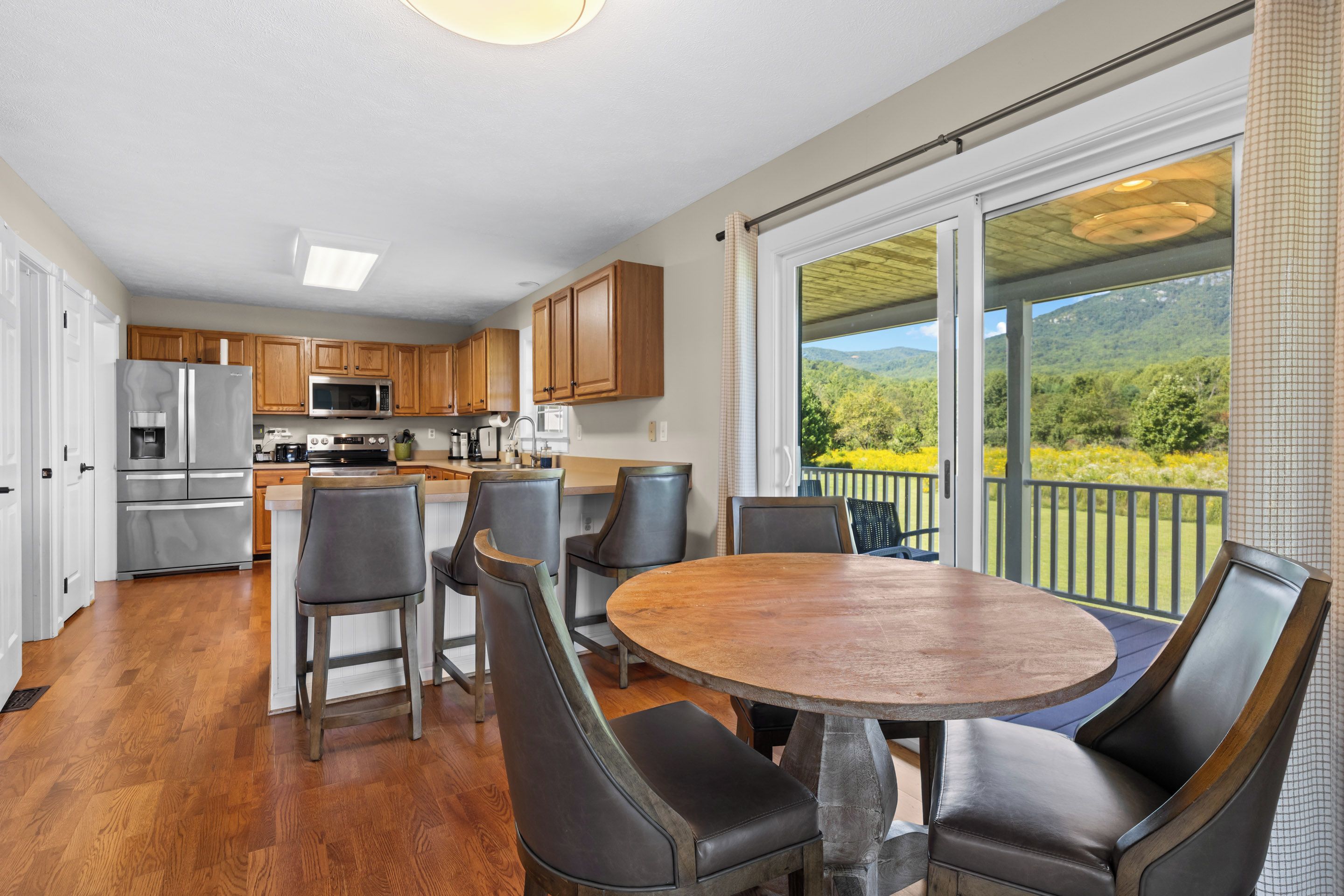A modern kitchen with stainless steel appliances, wooden cabinets, and a dining area with a round table and leather chairs.