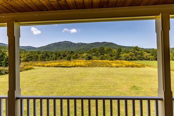 Eine überdachte Veranda mit Blick auf ein Wiesfeld und Berge.