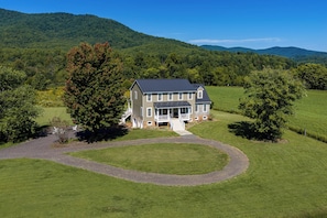 A two-story house with a large front porch and a driveway leading to the entrance.