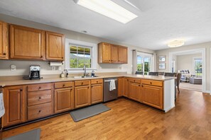 A modern kitchen with wooden cabinets, a built-in dishwasher, and a large window providing a view of the outdoors.