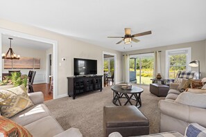 A spacious living room with a television, a ceiling fan, and a view of the outdoors.