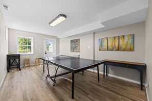 A room with a ping pong table, wooden flooring, a bench, and artwork on the wall.
