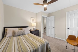 A bedroom with a bed, a nightstand, a lamp, a chair, and a door.