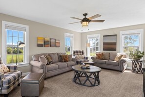 A spacious living room with a large sectional sofa, a round coffee table, and a ceiling fan.