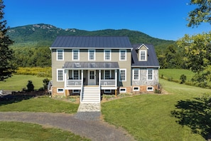 A two-story house with a front porch, a stone foundation, and a metal roof.