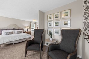 A bedroom with a bed, two armchairs, a small table with a plant, and a wall with framed pictures.