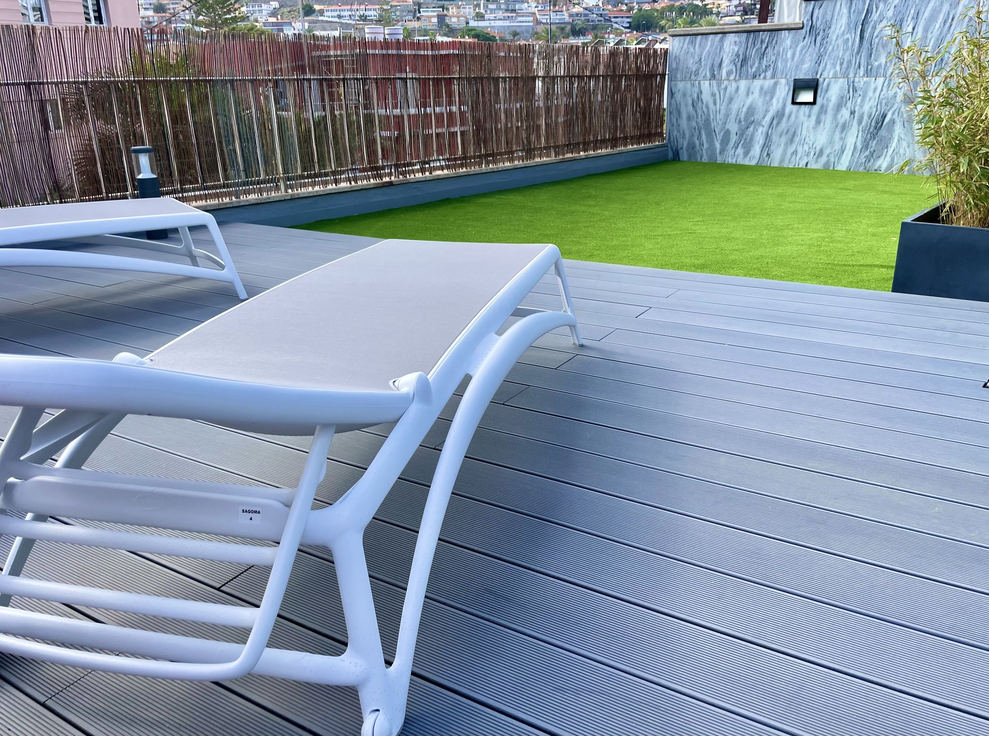 Eine Dachterrasse mit Holzboden, einer kleinen Fläche künstlichem Rasen und einem weißen Metallstuhl.