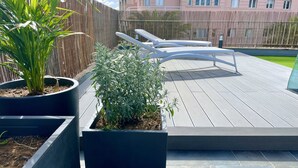 Une terrasse sur le toit agrémentée de plantes en pot, avec un espace salon et une vue sur un bâtiment en arrière-plan.