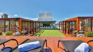Een dakterras met loungestoelen en een groen tapijt, met uitzicht op een modern gebouw.