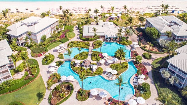 A resort with a central swimming pool, multiple guest buildings, and a beach. - BEST LOCATION on Grace Bay! The Plaza at Ocean Club West! No Car Needed! (Grace Bay)