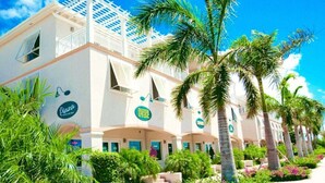 A hotel with a white facade, multiple balconies, and palm trees. - BEST LOCATION on Grace Bay! The Plaza at Ocean Club West! No Car Needed! (Grace Bay)