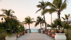 A wooden boardwalk leading to a beach with palm trees and outdoor seating. - BEST LOCATION on Grace Bay! The Plaza at Ocean Club West! No Car Needed! (Grace Bay)