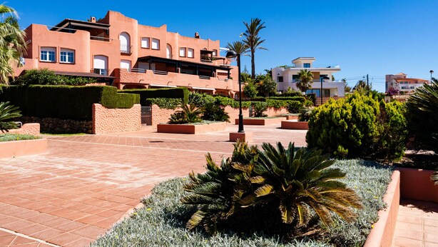Un edificio moderno con varios balcones y un patio amplio con jardines bien cuidados.