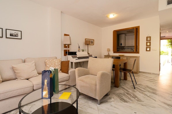 Una sala de estar con sofá, sillón, mesa de centro y piano.