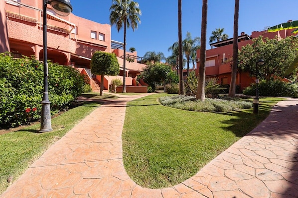 A pathway leading to a building with balconies, surrounded by well-maintained greenery and palm trees. - Alvarito Playa (Marbella)