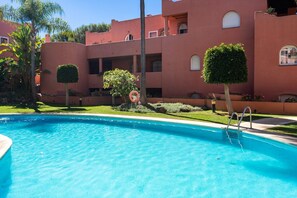Una piscina con superficie de agua azul cristalina, rodeada por un edificio con balcones y un césped bien cuidado.