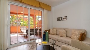 Una sala de estar con un sofá, una mesa de centro de vidrio y un ventanal corredero que da a un patio exterior.