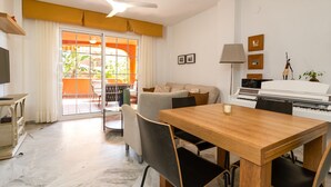 Una sala de estar con una mesa de comedor, sillas, un sofá, un piano y un televisor.