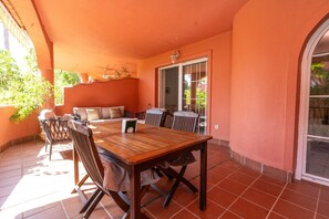 An outdoor patio with a wooden table and chairs, a sofa, and a sliding glass door leading to a garden. - Alvarito Playa (Marbella)