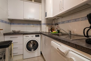 Una cocina compacta con lavadora, lavaplatos y armarios.