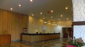 Un vestíbulo de hotel con una recepción, paredes de paneles de madera, piso estampado y lámparas colgantes.