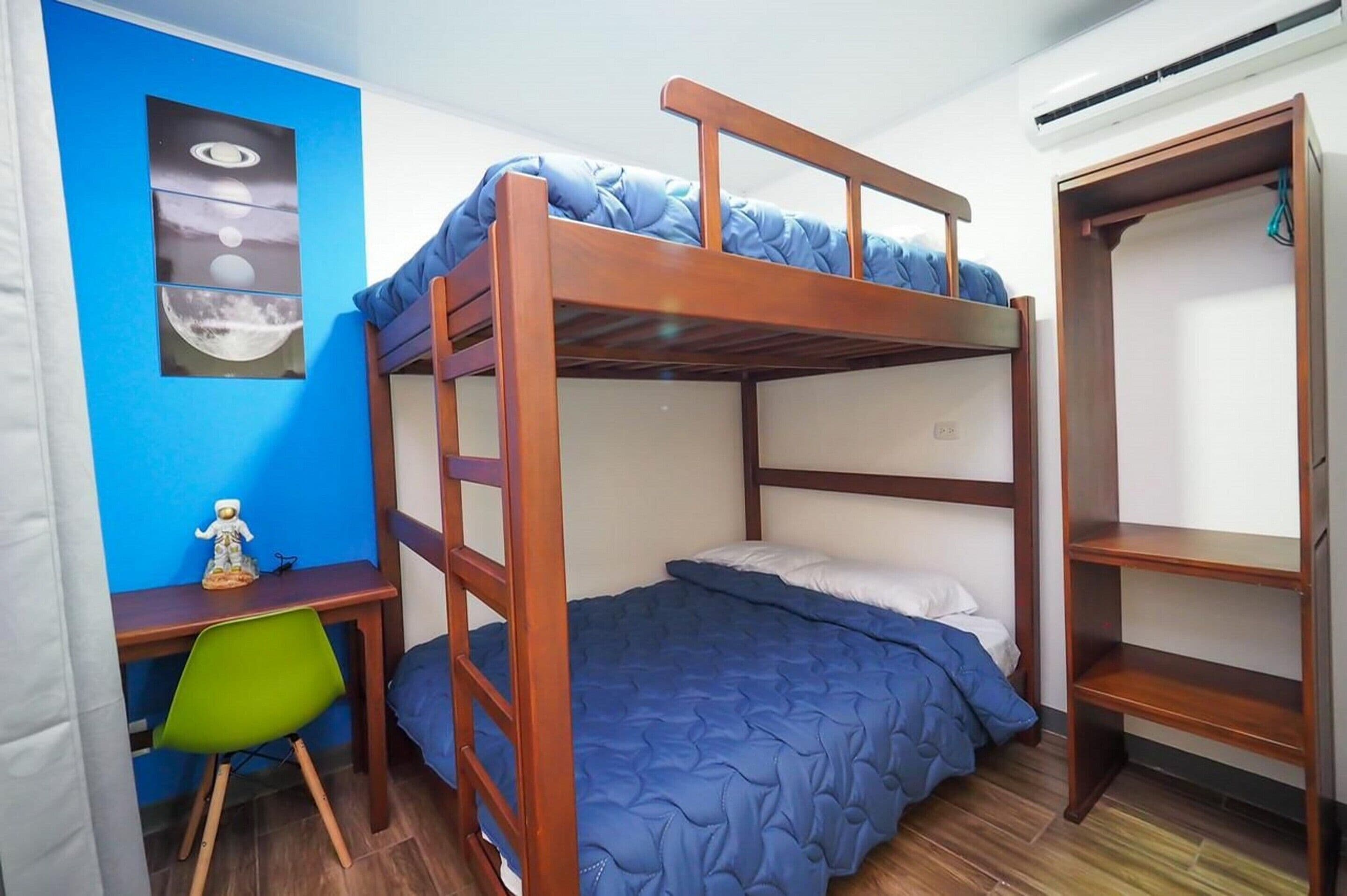 A bunk bed room with a desk and chair, a shelf, and a wall with a space-themed artwork.