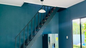 Una cocina moderna con un refrigerador de acero inoxidable, una escalera con barandilla de vidrio y vistas al exterior a través de una puerta de cristal.