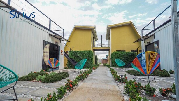 Una entrada de hotel con un camino central bordeado por sillas coloridas y follaje.