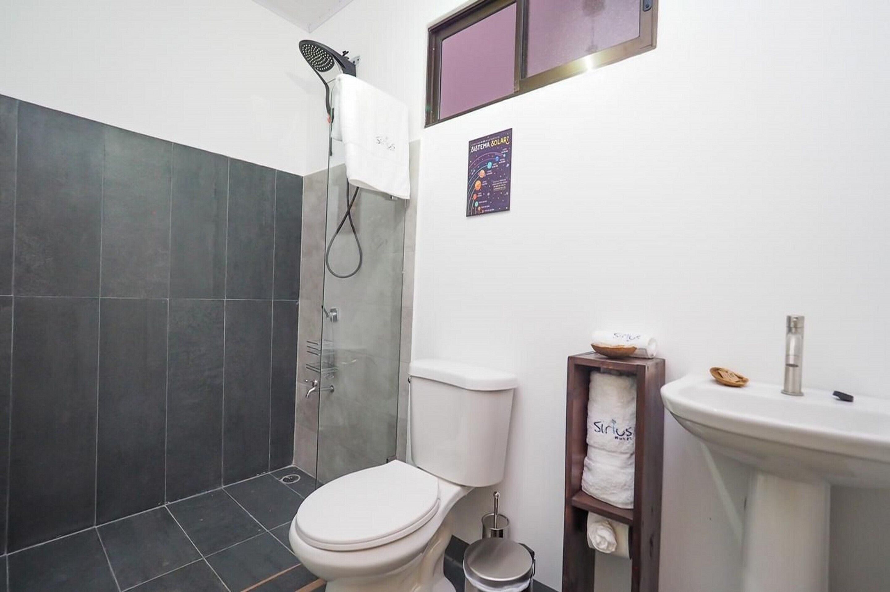 A bathroom with a shower, toilet, sink, and a poster on the wall.