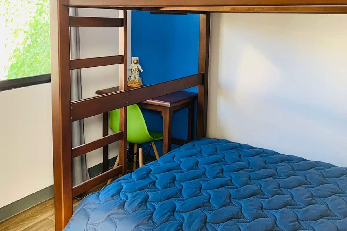 Una litera con colchón azul, estructura de madera y un escritorio pequeño con una silla.