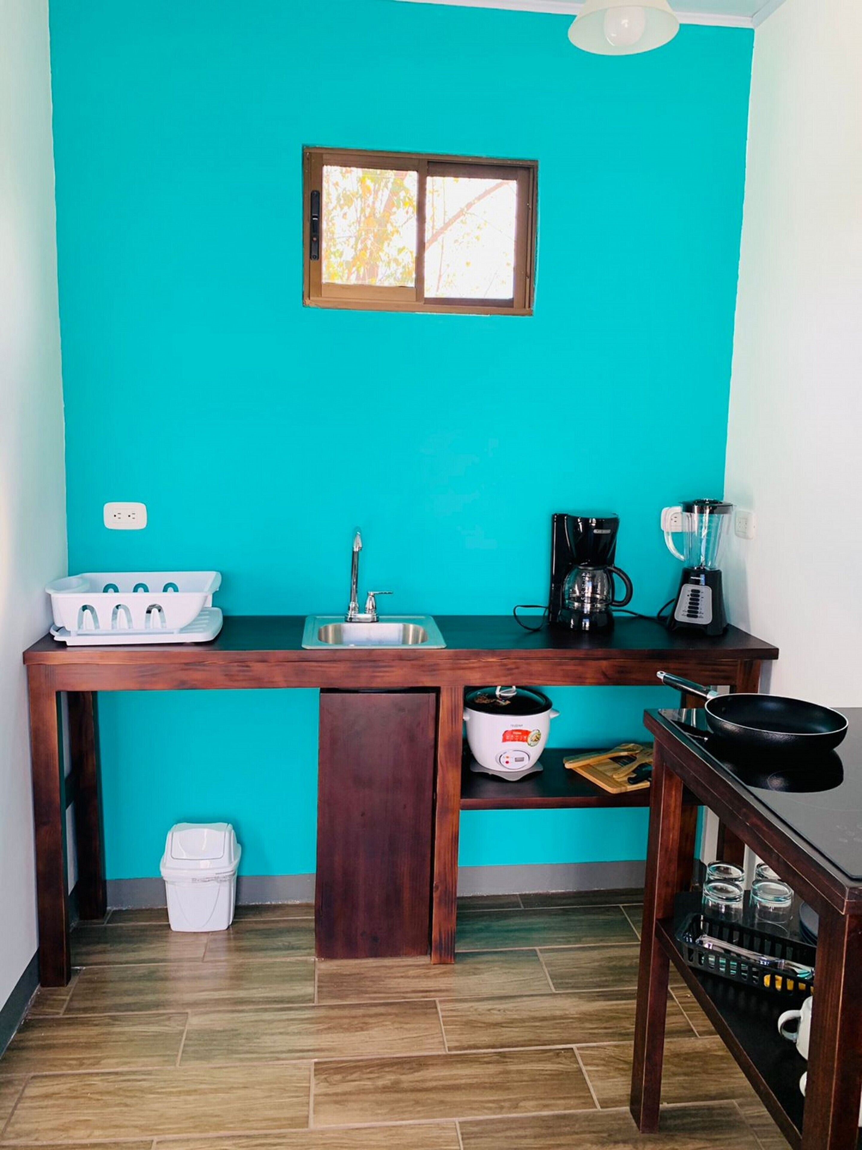 A compact kitchen with a teal wall, a wooden countertop, a sink, a stove, a coffee maker, and a small dining area.
