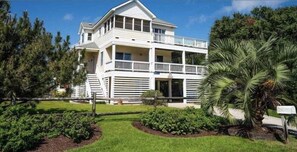 Une maison à deux étages dotée d’un balcon, entourée de verdure et d’une pelouse bien entretenue.