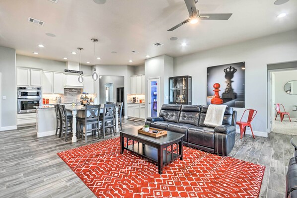 A modern kitchen with white cabinets, a dining area with a red patterned rug, and a living room with a leather sofa and a large red and white patterned rug.