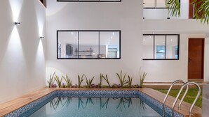 A modern indoor pool with clear glass walls, wooden deck, and metal pool ladder.