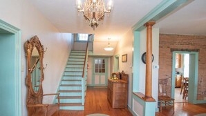 Una escalera que sube a un segundo piso, un banco de madera, un candelabro y una pared de ladrillo.