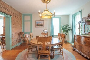 A dining room with a brick wall, wooden chairs, a round table, a chandelier, and a dresser with a mirror.