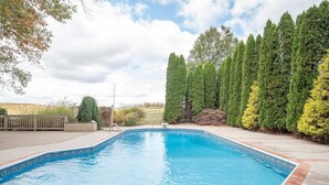 Una piscina rectangular con borde de azulejos, rodeada por una terraza de madera y varios árboles.