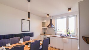 Cocina compacta con estufa, lavamanos y ventana. Hay un comedor con sillas y una mesa.