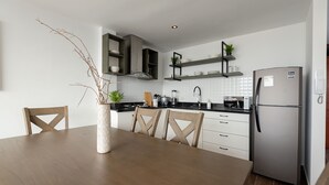 A modern kitchen with white cabinets, a stainless steel refrigerator, and a wooden dining table with chairs. - Departamento En La Playa De Estreno Con Piscina (Punta Hermosa)