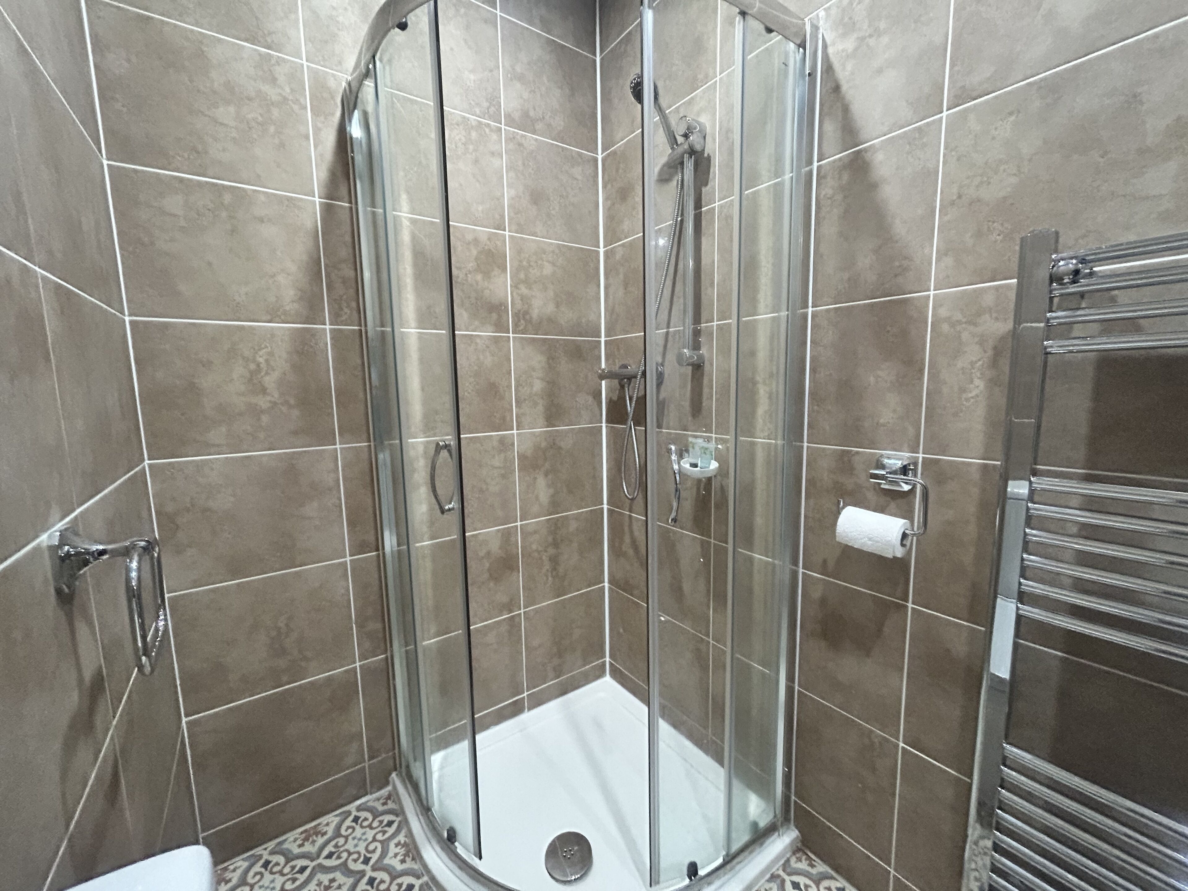 A glass-enclosed shower stall with a handheld showerhead and a wall-mounted faucet.