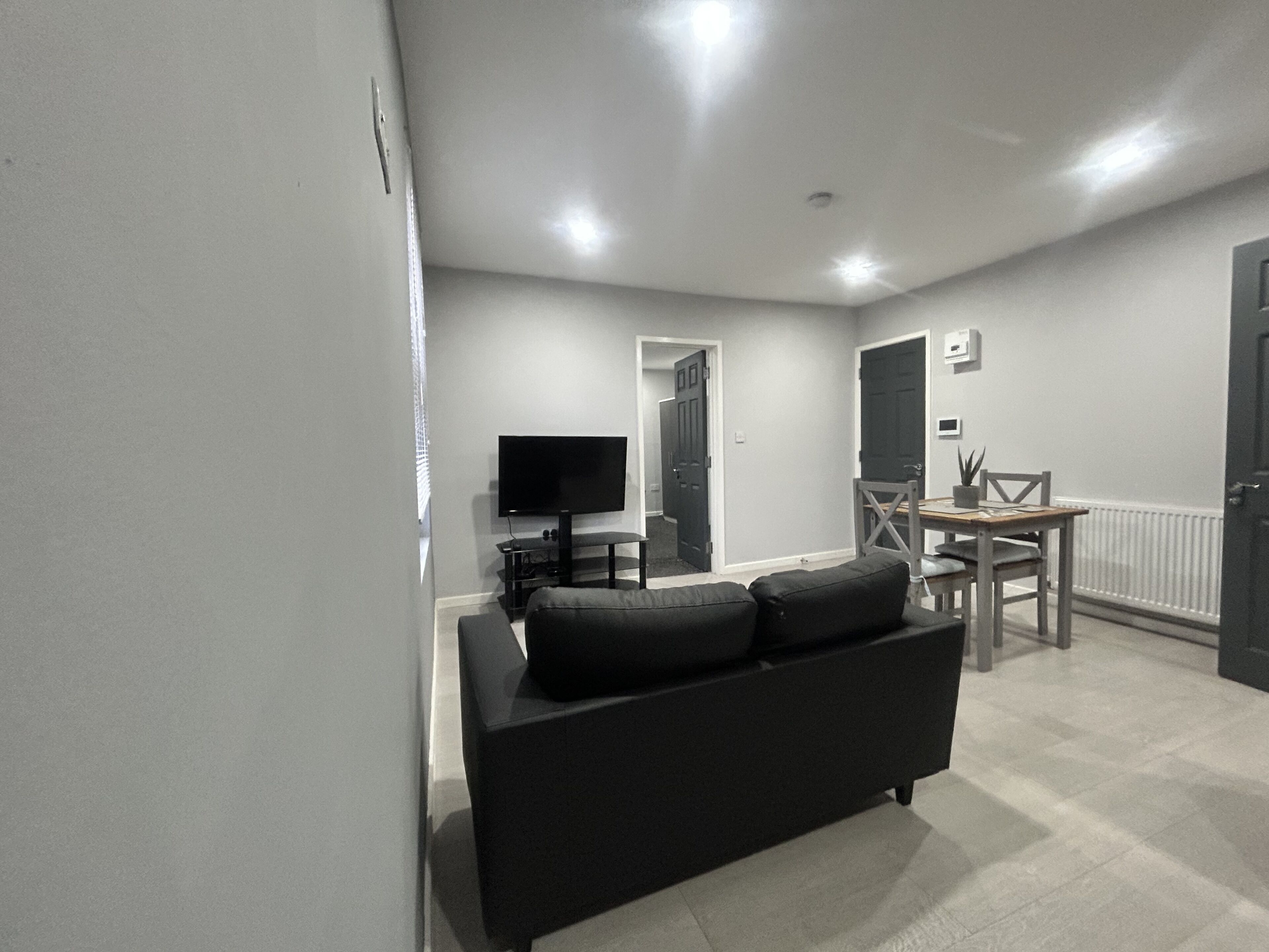A modern living room with a black sofa, a flat-screen TV, and a dining area with a table and chairs.