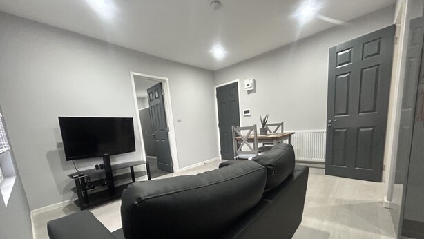 A modern living room with a black sofa, a flat-screen TV, and a dining area with a table and chairs. - Private Luxury Apartment - Free Parking & Wi-fi (Coventry)